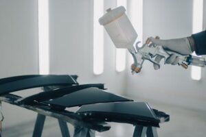 Home Close-up of car parts being spray-painted in an automotive workshop.